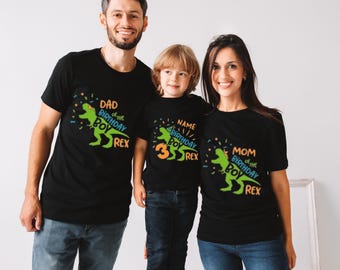 May include: A family of three wearing black t-shirts with a dinosaur graphic and text that says "Dad of the Birthday Boy Rex", "Name Birthday Boy 3 Rex", and "Mom of the Birthday Boy Rex".