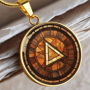 May include: Gold-toned pendant necklace with a circular design. The pendant features a mosaic-style pattern in shades of brown and gold, with a central triangle. The necklace has a delicate chain.