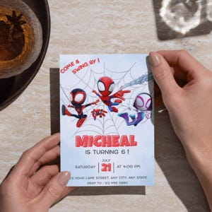Może przedstawiać: Jasnoniebieska karta zaproszenia z trzema postaciami Spider-Mana na białym tle pajęczyny. Na karcie widnieje napis "MICHEAL MA 6 LAT!" ze szczeg&oacute;łami daty i godziny. Karta jest trzymana przez osobę.