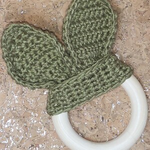 May include: A green crocheted bunny rabbit teether attached to a white wooden ring.