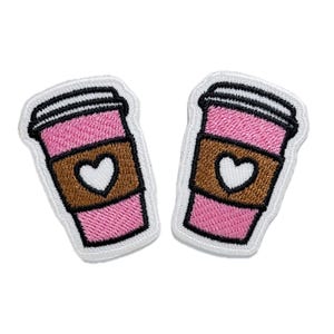 Könnte beinhalten: Zwei gestickte Bügelbilder in Form von Kaffeetassen, rosa und braun, mit einem weißen Herz auf dem braunen Band.