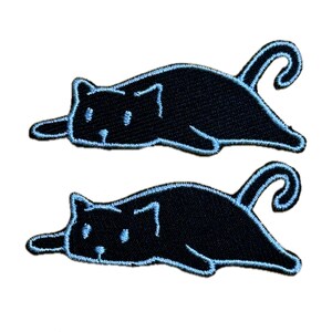 Puede incluir: Dos parches negros con forma de gato con contornos azul claro. Los gatos están en una pose relajada, con las colas enroscadas. Los parches son bordados y adecuados para ropa o accesorios.
