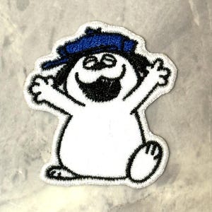 Puede incluir: Parche bordado con un personaje de dibujos animados con cuerpo blanco, contorno negro y gorro azul. El personaje tiene la boca abierta y los brazos levantados, dando una apariencia alegre. El parche está diseñado para planchar.