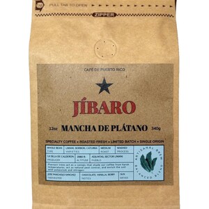 May include: A brown paper bag with a zipper closure. The bag contains 12 ounces of Mancha de Platano coffee, a single origin, limited batch, roasted fresh coffee from Puerto Rico. The bag features the brand name "Jibaro" and details about the coffee beans, including the type, varieties, roast, and process. The bag also includes information about the producer, altitude, pueblo, and harvest notes.