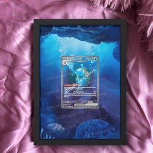 May include: A framed print featuring a Blastoise EX Pokémon card set against a blue underwater scene with bubbles and coral. The black frame contrasts with the vibrant card and background. Text at the bottom reads "card is not included."