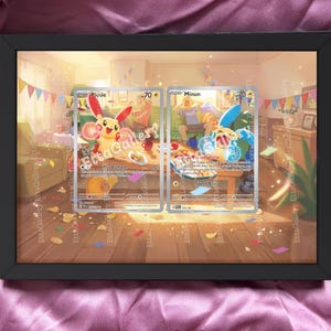 Könnte beinhalten: Ein gerahmter Druck mit zwei Pokémon-Sammelkarten, Plusle und Minun, vor einem farbenfrohen Hintergrund. Die Karten werden in einem schwarzen Rahmen mit einer Raumszene und Dekorationen präsentiert. Der Text unten lautet "cards are not included."
