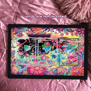 Puede incluir: Una exhibición enmarcada en negro con tres cartas de Pokémon. El marco está rodeado por un vibrante diseño floral con flores rosas, naranjas y azules. El texto "cards are not included" es visible en la parte superior.