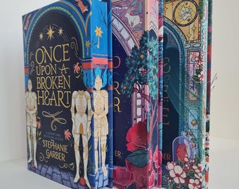 May include: A stack of hardcover books with colorful, illustrated covers. The first book features the title "Once Upon a Broken Heart" by Stephanie Garber. The covers display fantasy art with figures, floral designs, and a stained-glass window motif.