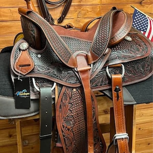 May include: A brown leather saddle with intricate floral tooling and a black woven pattern. The saddle is accompanied by a matching brown leather bridle with a woven pattern.