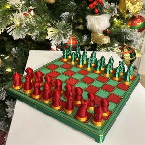 May include: A Christmas-themed chess set with red and green pieces and a matching board. The chess pieces are in the shape of Christmas-themed objects. The board is green with red squares. The set is displayed in front of a decorated Christmas tree.