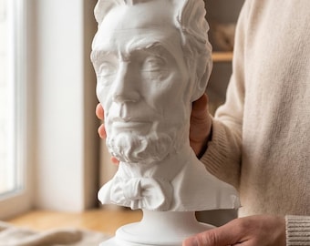 May include: A white matte bust sculpture of Abraham Lincoln featuring detailed facial features, a bow tie, and a collar. The sculpture is mounted on a rectangular base with the name Abraham Lincoln clearly engraved on the front edge of the base.