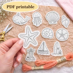 May include: A collection of PDF printable sea-themed designs, including a whale, jellyfish, seashell, starfish, and sailboat. The designs are outlined in black on a textured white material. The image also includes embroidery floss and scissors.