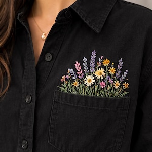 Könnte beinhalten: Schwarzes Jeanshemd mit floraler Stickerei auf der Tasche. Die Stickerei zeigt eine Vielzahl bunter Blumen, darunter Gänseblümchen und Lavendel. Das Hemd hat ein klassisches Knopfdesign.
