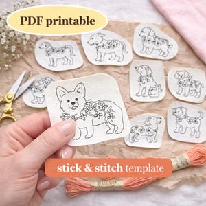 May include: A selection of white fabric patches featuring black line drawings of dogs with floral details. The patches are displayed on a brown surface, with the text "PDF printable" and "stick & stitch template". Peach embroidery floss and scissors are also present.