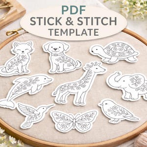 May include: A PDF stick and stitch template featuring various animal designs, including a cat, dog, turtle, dolphin, giraffe, elephant, hummingbird, butterfly, and bird. Each animal is decorated with floral patterns. The template is set on an embroidery hoop.