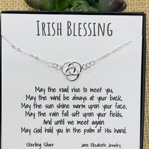 May include: A silver Celtic knot necklace with a card that reads "Irish Blessing" and includes a poem: "May the road rise to meet you, May the wind be always at your back, May the sun shine warm upon your face, May the rain fall soft upon your fields, And until we meet again May God hold you in the palm of His hand." The card also states "Sterling Silver" and "Jane Elizabeth Jewellery".