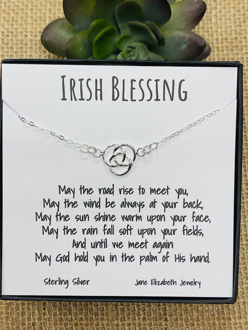 May include: A silver Celtic knot necklace with a card that reads "Irish Blessing" and includes a poem: "May the road rise to meet you, May the wind be always at your back, May the sun shine warm upon your face, May the rain fall soft upon your fields, And until we meet again May God hold you in the palm of His hand." The card also states "Sterling Silver" and "Jane Elizabeth Jewellery".