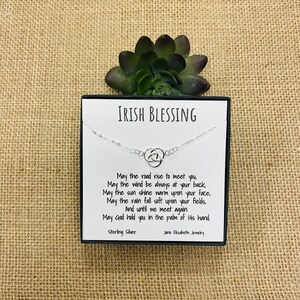 May include: A silver necklace with a Celtic knot charm and a card with an Irish blessing. The card reads: "May the road rise to meet you, May the wind be always at your back, May the sun shine warm upon your face, May the rain fall soft upon your fields, And until we meet again May God hold you in the palm of His hand. Sterling Silver Jane Elizabeth Jewellery"
