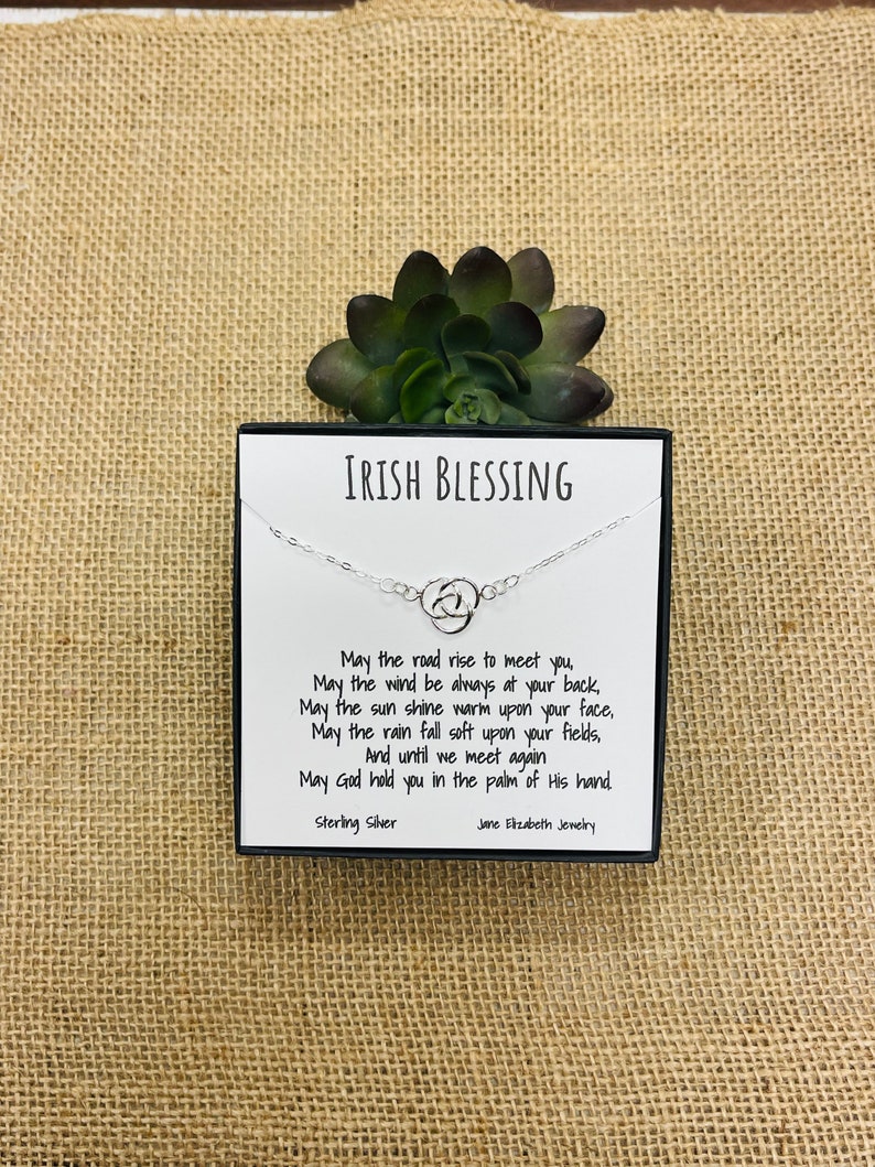 May include: A silver necklace with a Celtic knot charm and a card with an Irish blessing. The card reads: "May the road rise to meet you, May the wind be always at your back, May the sun shine warm upon your face, May the rain fall soft upon your fields, And until we meet again May God hold you in the palm of His hand. Sterling Silver Jane Elizabeth Jewellery"