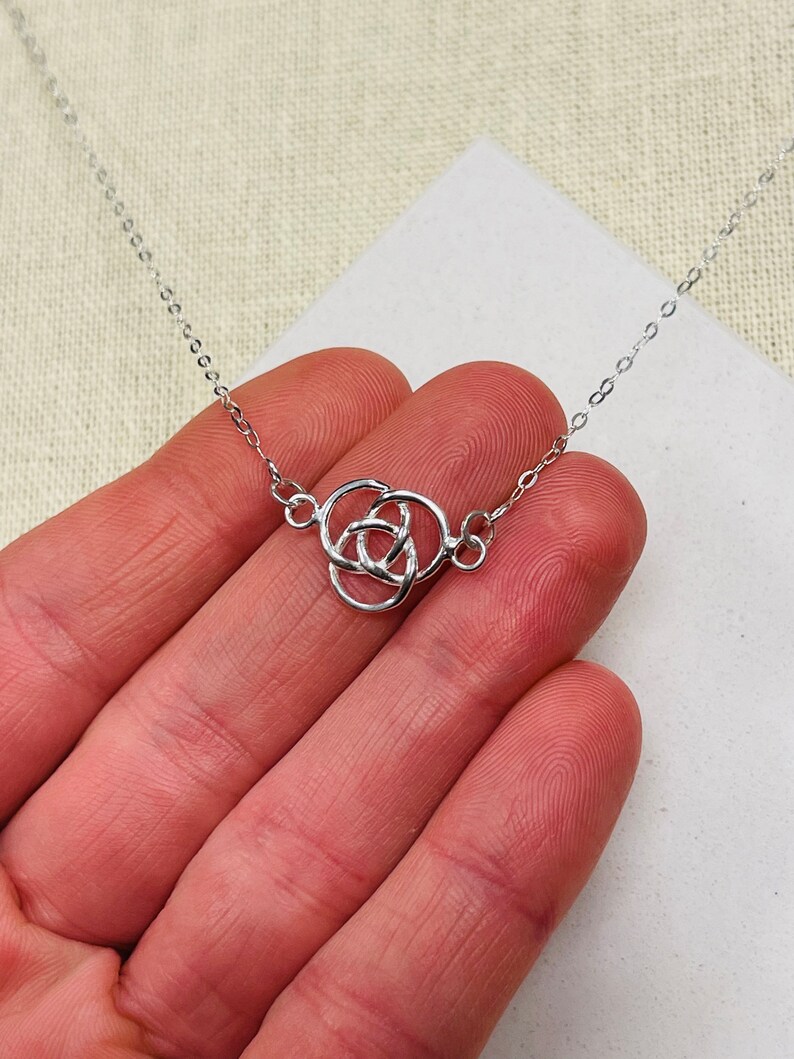 May include: A silver chain necklace with a Celtic knot pendant. The pendant is a simple design with three interlocking circles.