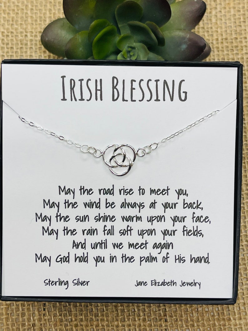 May include: A silver Celtic knot necklace with a card that reads "Irish Blessing" and includes a poem: "May the road rise to meet you, May the wind be always at your back, May the sun shine warm upon your face, May the rain fall soft upon your fields, And until we meet again May God hold you in the palm of His hand." The card also states "Sterling Silver" and "Jane Elizabeth Jewellery".