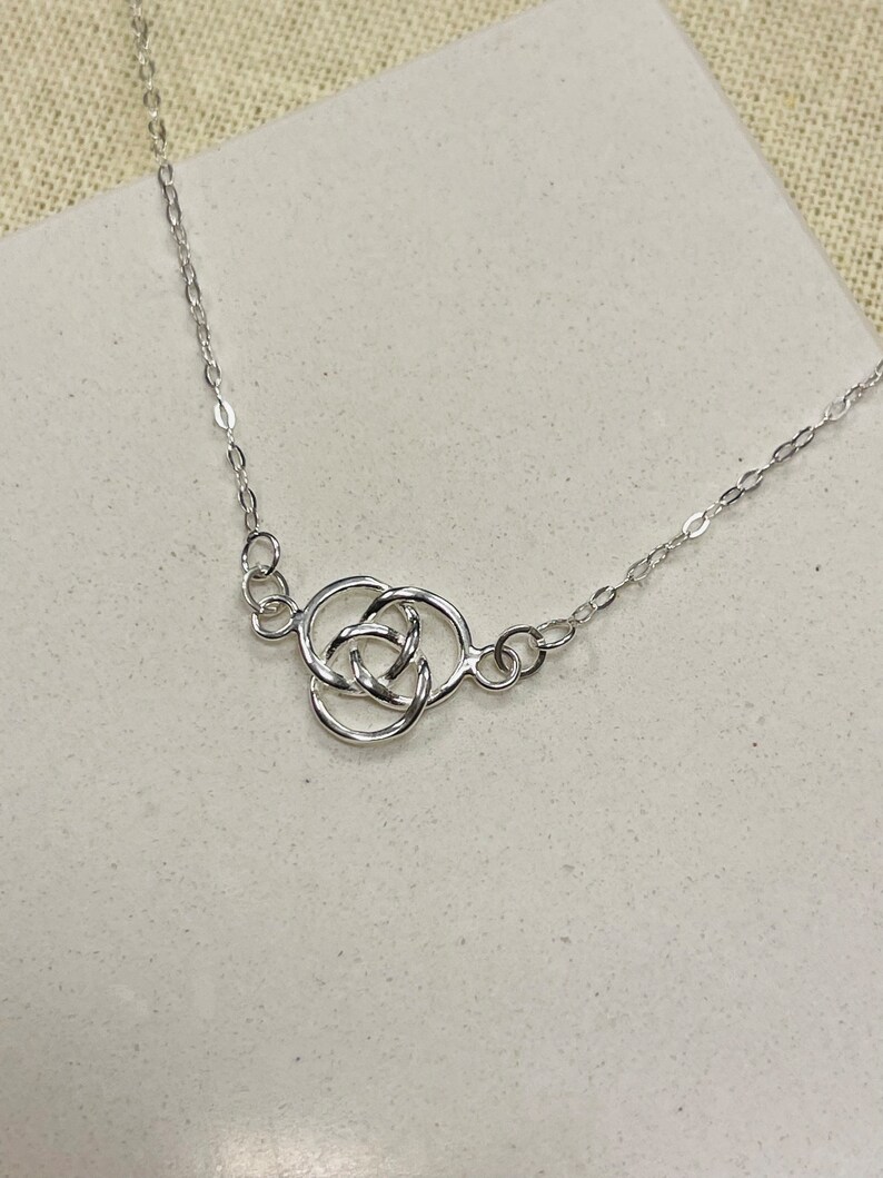 May include: A silver necklace featuring a Celtic knot pendant. The knot is formed from three interlocked circles.