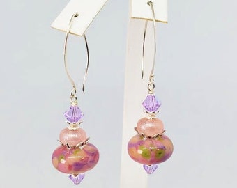 Peut inclure: Une paire de boucles d'oreilles pendantes avec des perles de verre roses et violettes et des accents de cristal. Les boucles d'oreilles sont en argent et ont une fermeture à crochet.