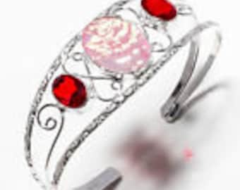 Peut inclure: Bracelet manchette en argent avec une rose rose et deux pierres précieuses rouges. Le bracelet a un design délicat et orné.