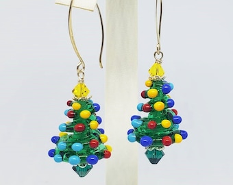 Peut inclure: Une paire de boucles d'oreilles pendantes avec un motif de sapin de Noël en perles vertes, rouges, jaunes et bleues. Les boucles d'oreilles sont en métal doré et ont une goutte de cristal au bas.
