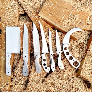 May include: A collection of stainless steel knives with white handles, including a cleaver and a curved blade, displayed on a wooden surface with a black leather sheath. The knives vary in size and shape.