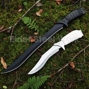 May include: Two knives with curved blades rest on a bed of green moss and leaves. One knife has a black blade and handle, while the other has a white blade and handle. The handles are wrapped for grip.