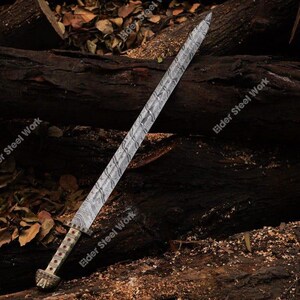 May include: A long, ornate sword with a patterned blade and a decorative handle. The blade has a silver and gray design. The handle features red and gold accents. The sword is displayed on a bed of wood and leaves.