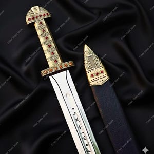 Puede incluir: Una espada decorativa con empuñadura y detalles dorados, adornada con piedras preciosas rojas. La hoja es plateada con marcas grabadas. La espada descansa sobre una superficie negra texturizada, con una vaina a juego.