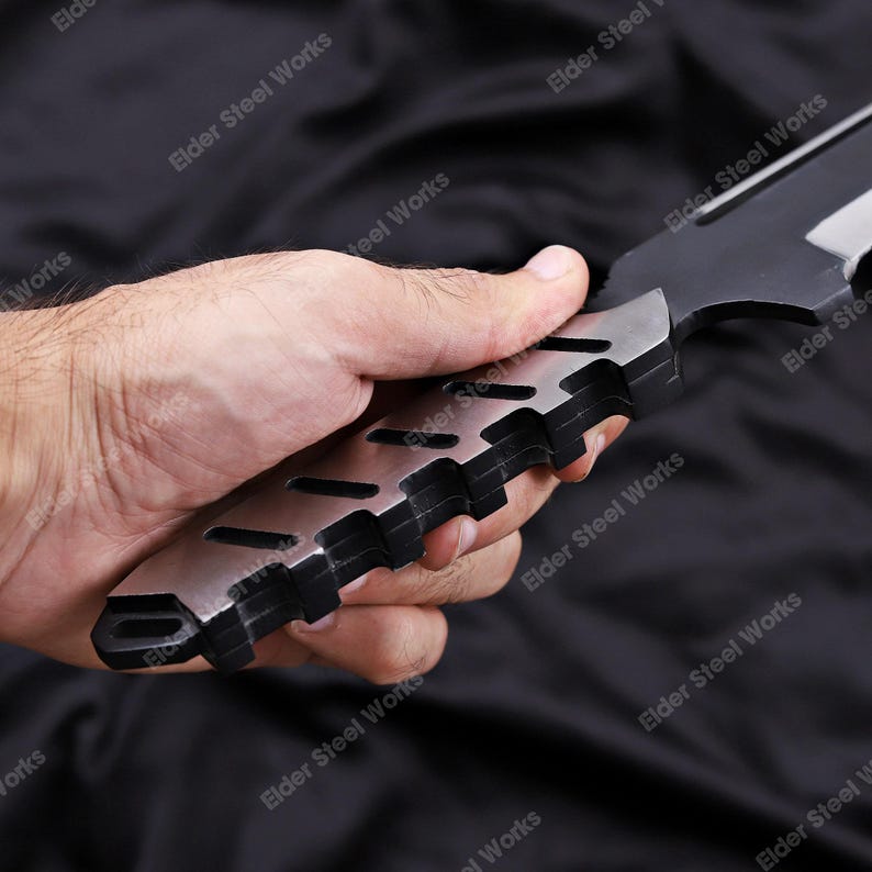 May include: A black and silver knife with a textured handle is held in a hand. The handle has a series of cut-out sections. The blade is black with a silver edge. The knife is labeled "Elder Steel Works".