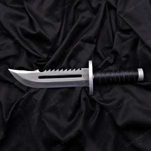 May include: A stainless steel survival knife with a serrated spine and a black wrapped handle. The blade has a sharp edge and a fuller. The knife is displayed on a black satin background.