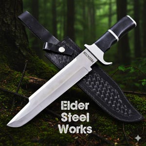 May include: A large, silver blade knife with a black handle and a black leather sheath. The knife is labeled "PREDATOR" and the sheath is embossed with a pattern. The text "Elder Steel Works" is displayed below the knife.