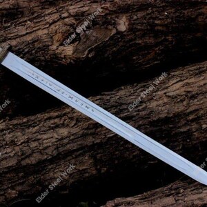 May include: A long, silver sword with a decorative handle featuring red and gold accents. The blade has etched markings and is displayed against a textured, brown wooden surface. The words "Elder Steel Work" are visible.