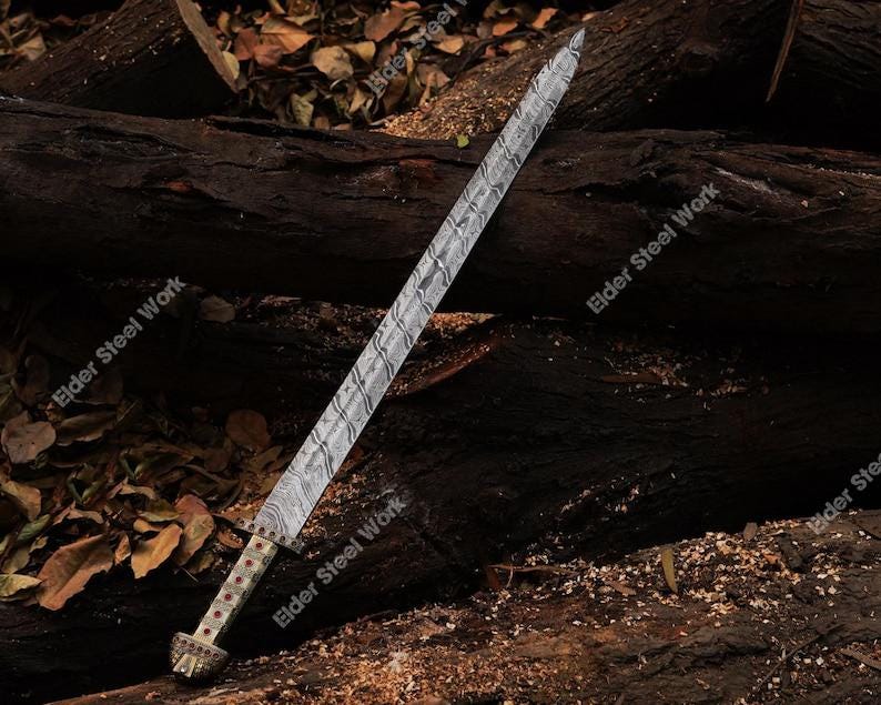 May include: A long, ornate sword with a patterned blade and a detailed hilt. The blade has a textured, wavy design. The hilt features red accents and a decorative pommel. The sword rests on a dark wooden surface.
