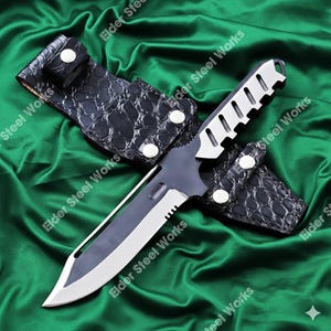May include: A tactical knife with a silver blade and a black handle, resting in a black leather sheath. The sheath has a crocodile skin texture and is secured with silver snaps. The knife is designed for outdoor use.