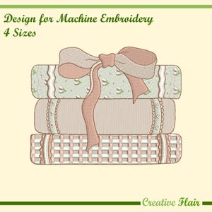 May include: Machine embroidery design featuring a stack of three embroidered books tied with a large bow. The books have detailed patterns in shades of pink, green, and cream. The text "Design for Machine Embroidery" and "4 Sizes" is visible.