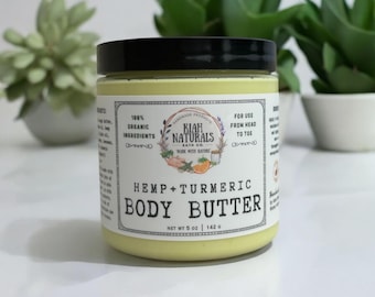May include: A yellow jar of hemp and turmeric body butter with a white label. The label says "Kiah Naturals Bath Co." and "Hemp + Turmeric Body Butter". The jar is sitting on a white surface.