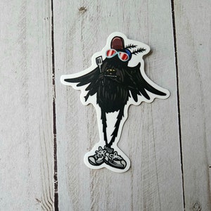 May include: A black sticker featuring a cartoon creature with sunglasses, a hat, and sneakers. The creature has wings and is holding a spatula. The sticker is on a white background with a wood grain pattern.