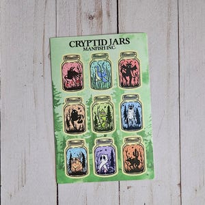 May include: A sticker sheet titled CRYPTID JARS MANFISH INC. featuring nine individual illustrations of mythical creatures enclosed in glass jars. Each jar contains a unique creature set against a colorful background with trees and natural elements.