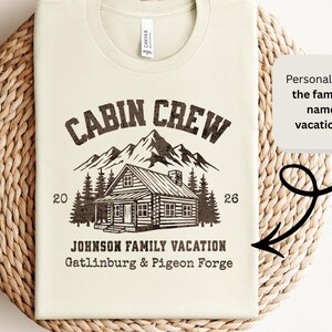 Puede incluir: Camiseta color crema con un gr&aacute;fico desgastado. Presenta el texto "CABIN CREW" sobre una ilustraci&oacute;n de caba&ntilde;a, monta&ntilde;as y &aacute;rboles. Debajo, se lee "JOHNSON FAMILY VACATION Gatlinburg & Pigeon Forge". La camiseta est&aacute; sobre una superficie tejida.