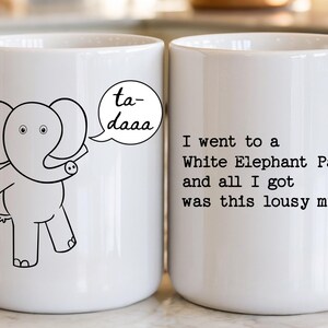 May include: Two white ceramic mugs featuring black line art. The left mug shows a cartoon elephant with a speech bubble saying ta-daaa. The right mug features the black text: I went to a White Elephant Party and all I got was this lousy mug.