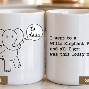 May include: A white ceramic mug featuring a black line drawing of an elephant with a speech bubble saying ta-daaa on one side and the black text I went to a White Elephant Party and all I got was this lousy mug on the other side.