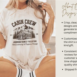 Puede incluir: Camiseta color crema con un gr&aacute;fico que presenta una caba&ntilde;a, monta&ntilde;as y el texto "CABIN CREW JOHNSON FAMILY VACATION Gatlinburg & Pigeon Forge". La camiseta se combina con un vaso de caf&eacute; helado.