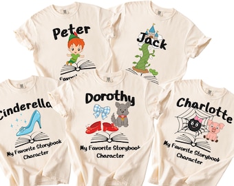 Pode incluir: Cinco t-shirts de cor creme com gráficos de contos de fadas. Cada t-shirt apresenta um nome, uma ilustração de um livro aberto e uma personagem ou objeto: Peter Pan, um pé de feijão com castelo, um sapato de cristal, Dorothy com sapatos vermelhos e um cão, e Charlotte com um porquinho.