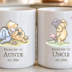 May include: Two white ceramic mugs with Winnie the Pooh illustrations. One mug features Pooh and Eeyore, the other Pooh and Piglet. Text on the mugs reads "Promoted to Auntie" and "Promoted to Uncle", with the year 2026.