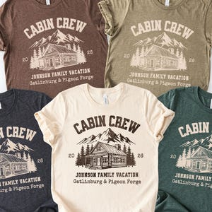 Puede incluir: Cinco camisetas de manga corta en varios colores, cada una con el texto "CABIN CREW" encima de un gr&aacute;fico de caba&ntilde;a y monta&ntilde;a. El texto "JOHNSON FAMILY VACATION Gatlinburg & Pigeon Forge" est&aacute; impreso debajo. Las camisetas son marrones, beige, grises, crema y verdes.